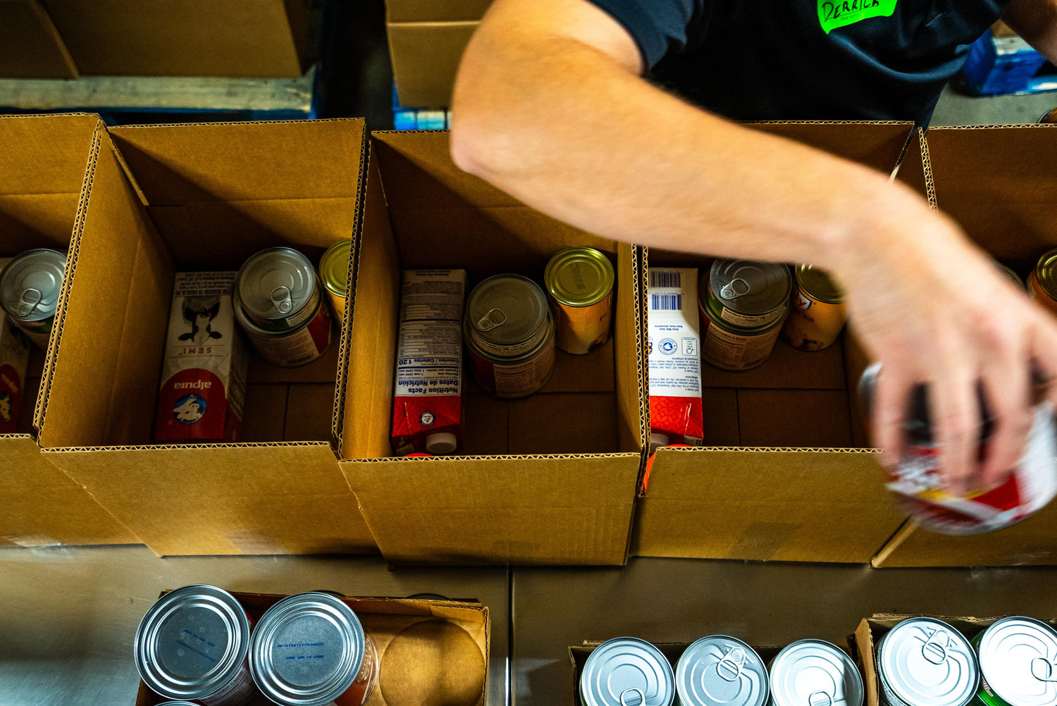 Volunteer packing boxes with canned food at Second Harvest Food Bank, demonstrating community support and hunger relief efforts.