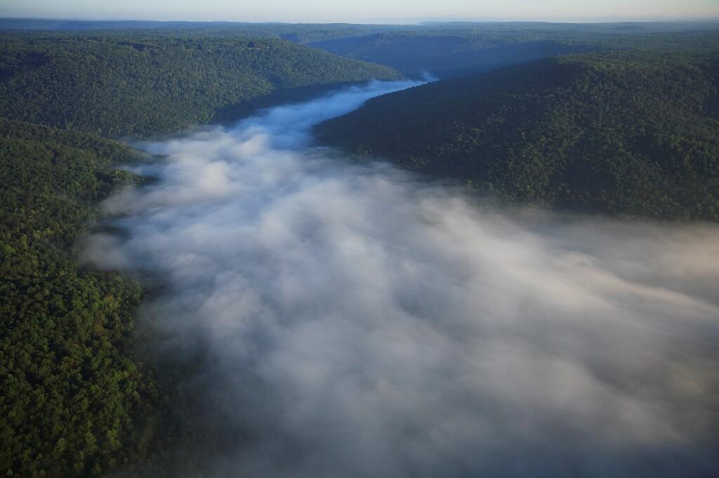 Aerial view of misty valley over Lost Cove, Tennessee, surrounded by lush green forested hills under a clear morning sky.