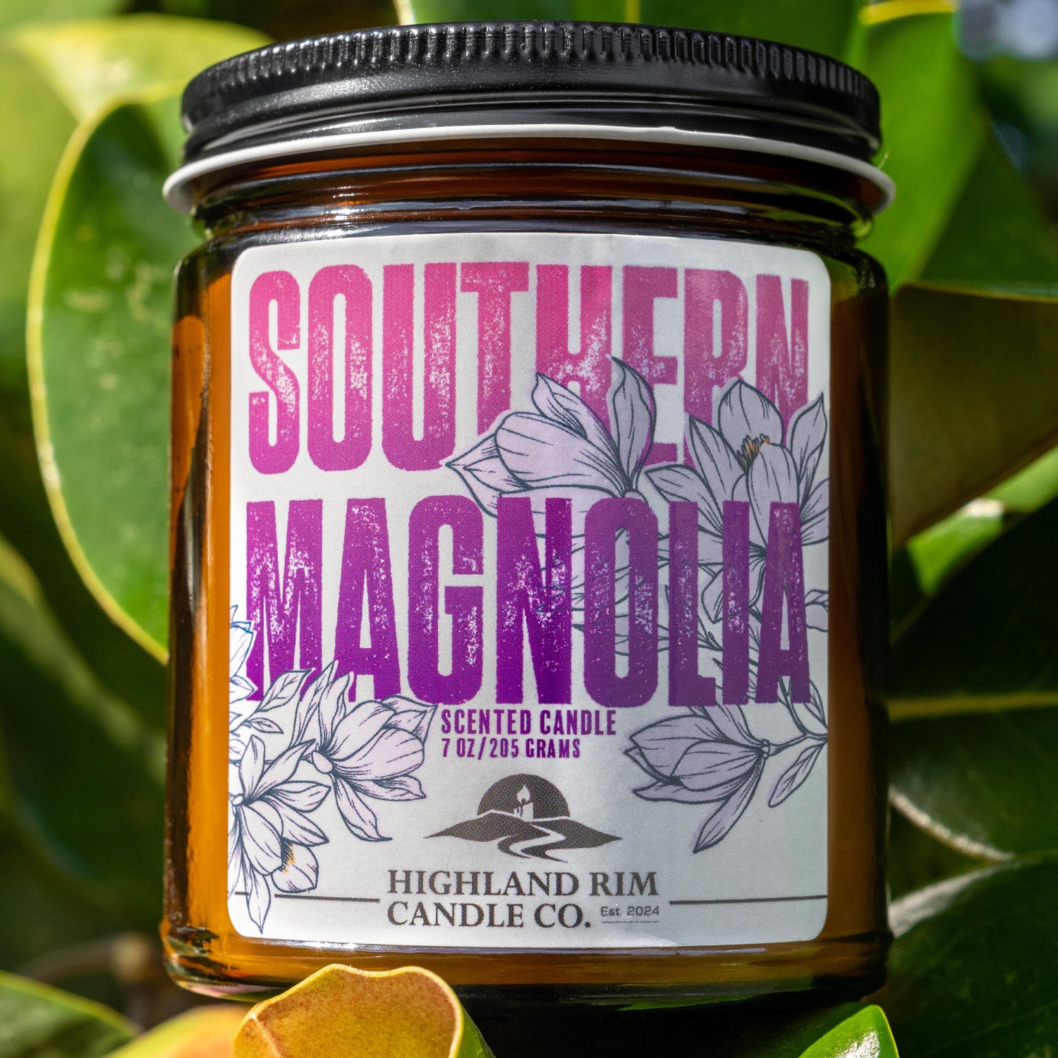 Southern Magnolia candle by Highland Rim Candle Co. nestled among magnolia leaves outdoors, capturing the essence of Tennessee's iconic magnolia flower.