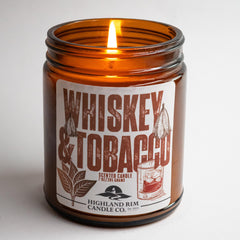 Amber glass Whiskey & Tobacco candle by Highland Rim Candle Co., lit in a studio setting, creating a warm, inviting glow with a classic label design.